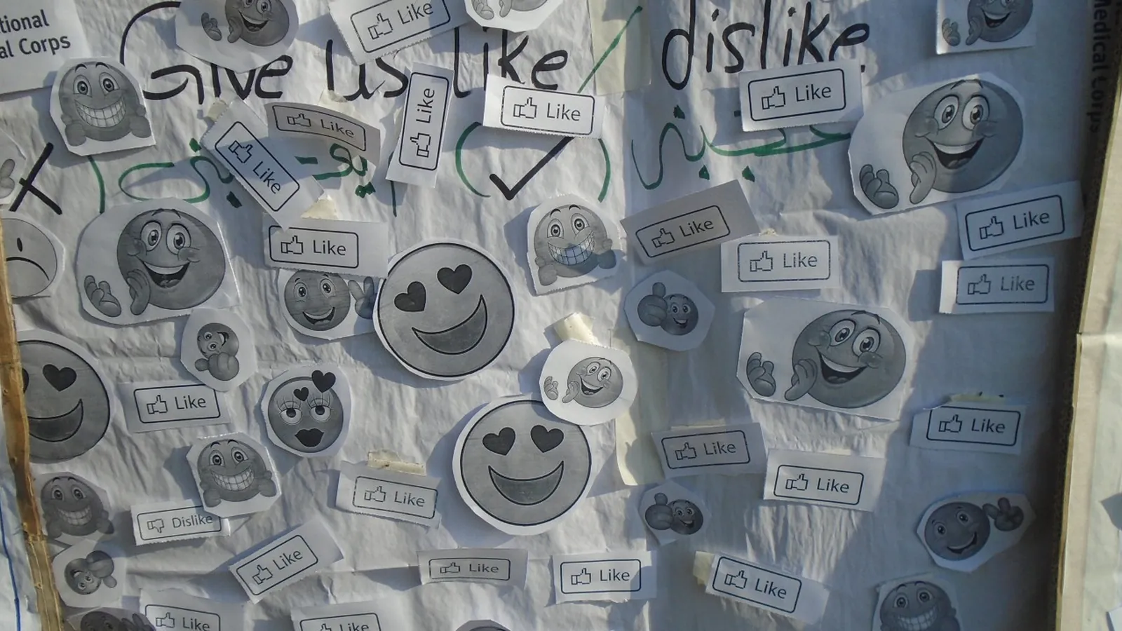 A wall papered with printed and hand drawn Like and dislike buttons and smiley faces.